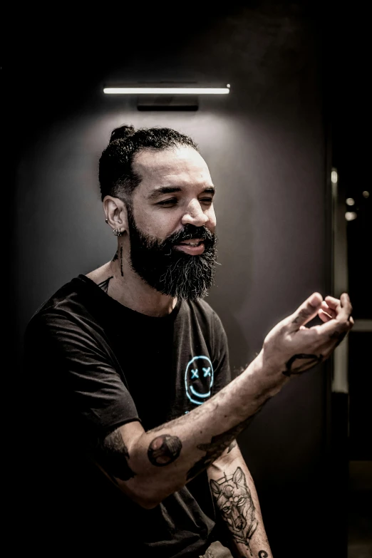 a man with a beard and tattoos sitting in front of a black wall