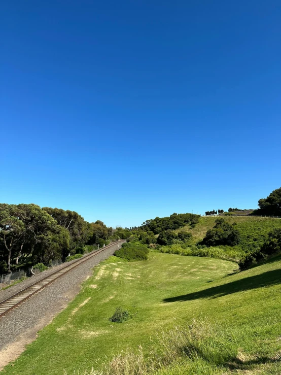 the green and grassy countryside has trees, bushes, and train tracks