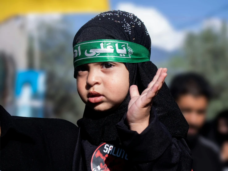 a little boy wearing a scarf, black shirt and scarf holding up his hand