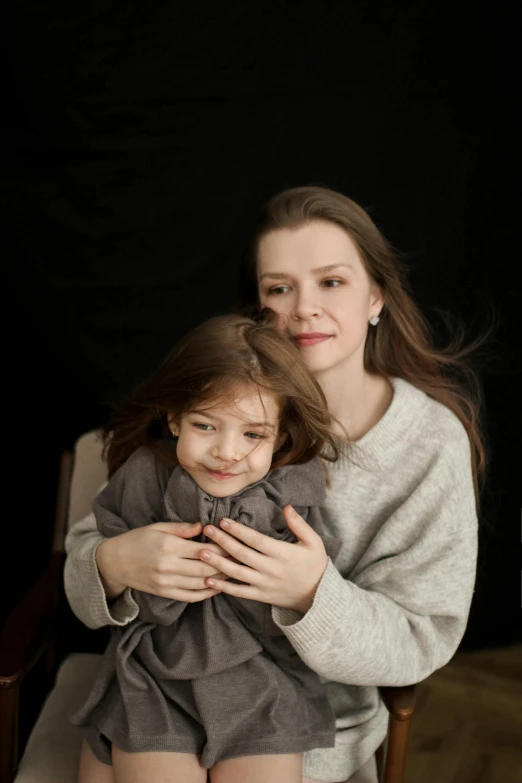 a woman holds a small child, with a chair behind her