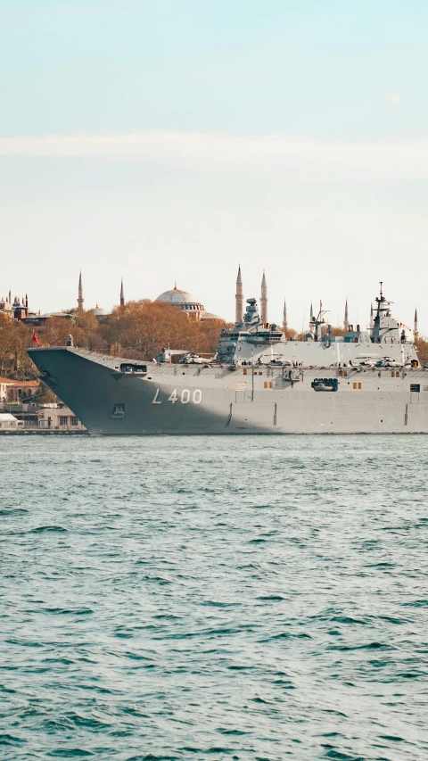 an aircraft carrier is moored on the water with city in the background