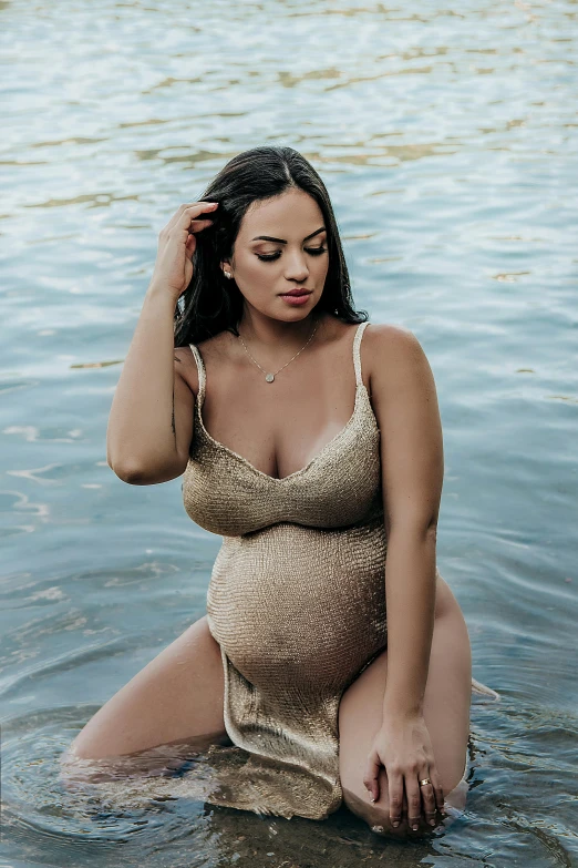 a pregnant woman in a lake wearing a gold swimsuit