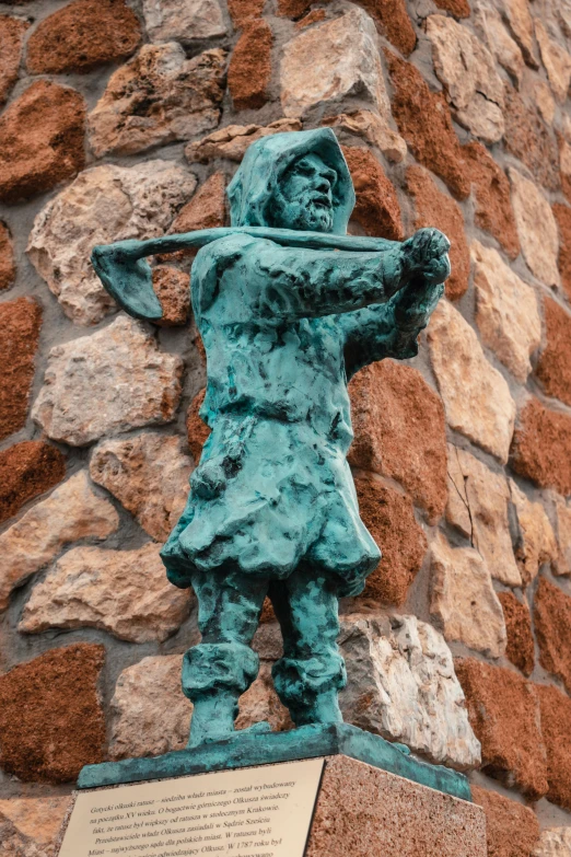 a bronze statue holding a long stick near a wall