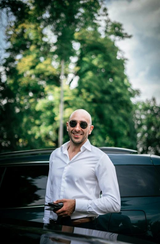 an older man posing with his car and holding a phone