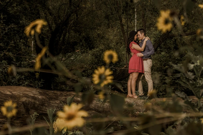 a young man is standing next to a young lady as they both kiss with flowers in the foreground