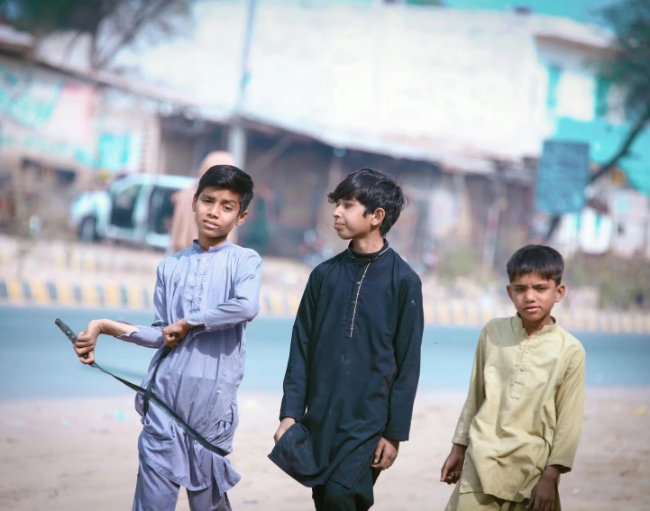 a group of three children holding sticks on a dirt ground