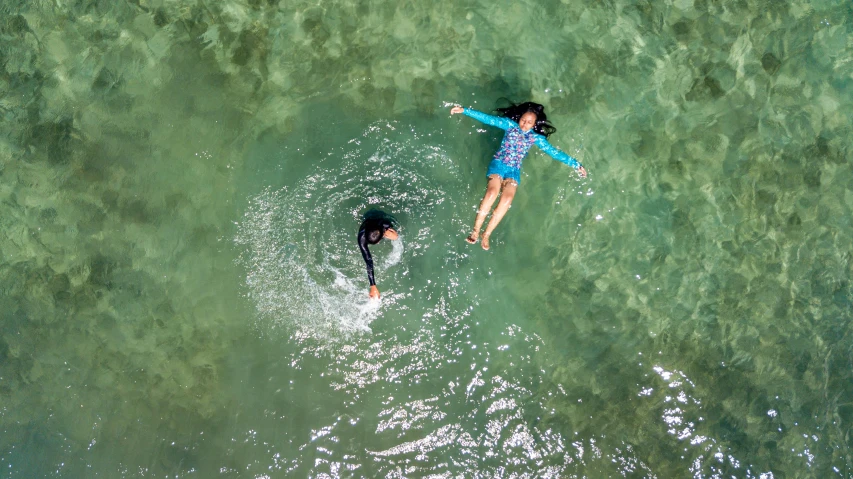 an aerial view of a woman riding a wave while another paddles nearby