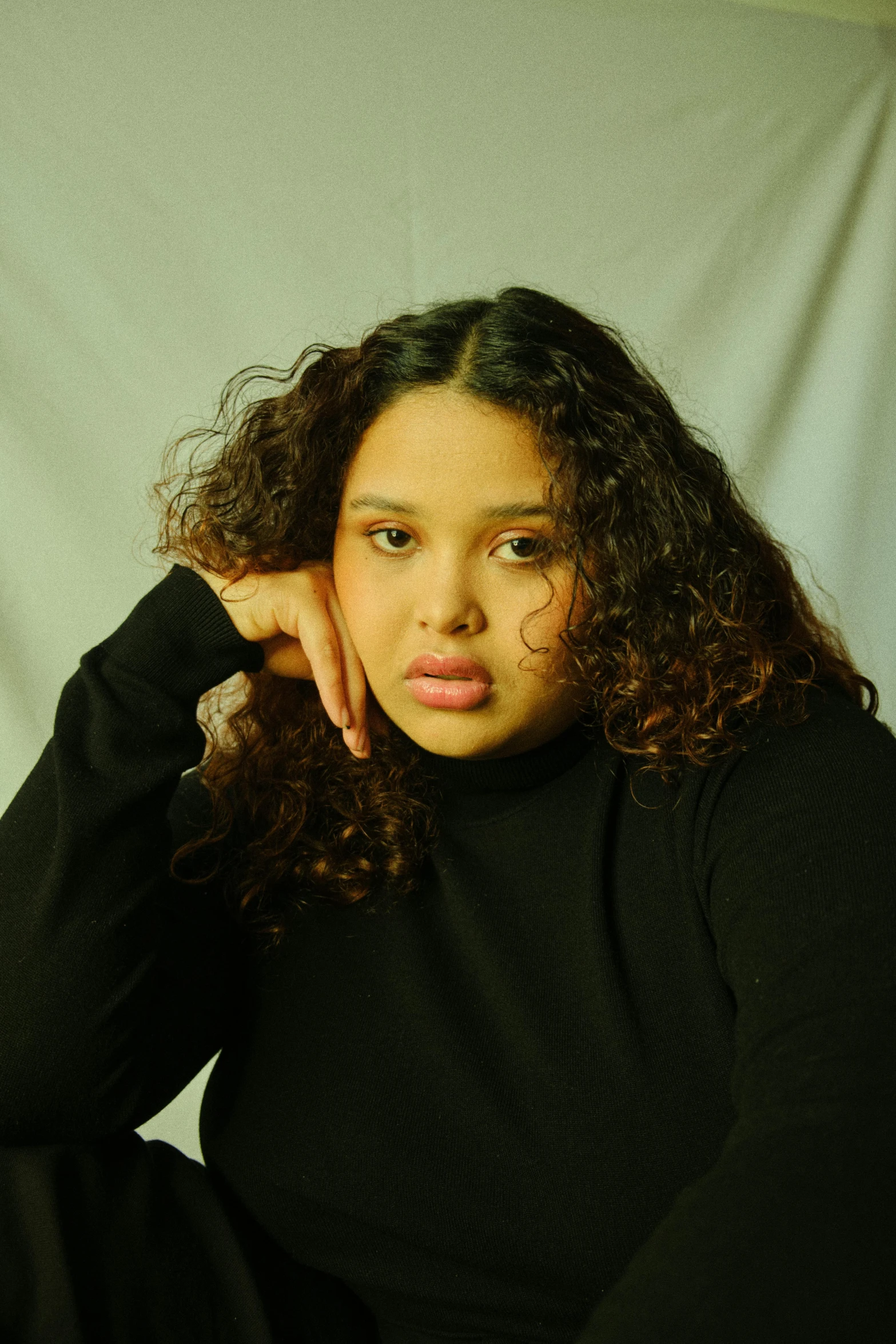 a woman with curly hair sitting down and posing for the camera