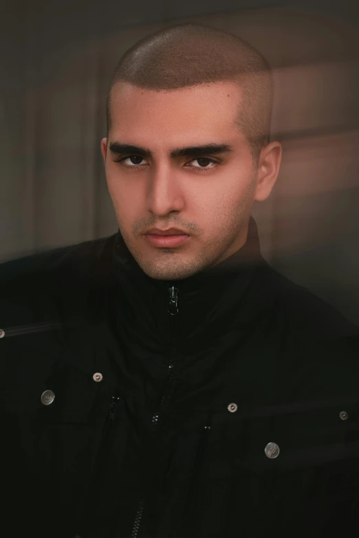 a young man with a bald and shaved head standing in front of a window