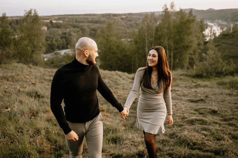 couple holding hands walking on grassy hill in the woods