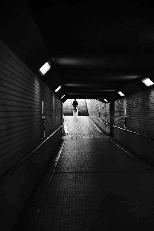 a person with an umbrella walking out the end of a tunnel