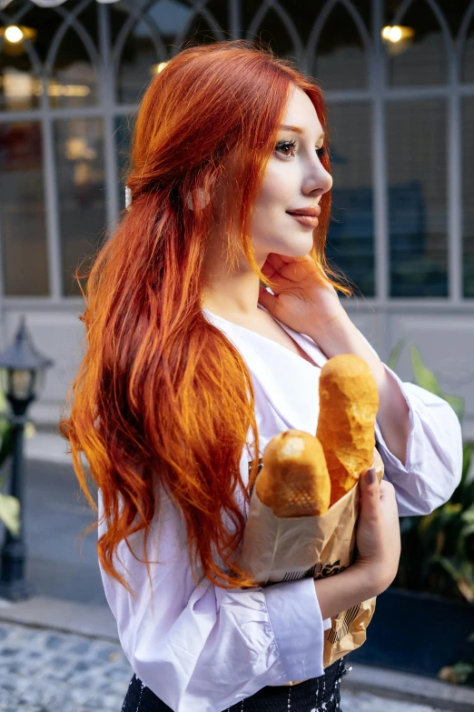 woman with red hair holding two breads in front of a building