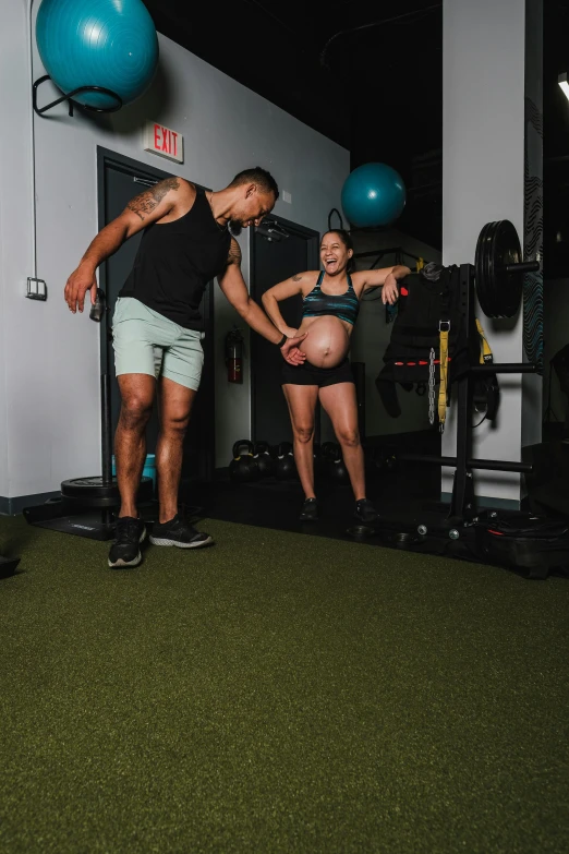 a pregnant lady standing next to a man in a gym