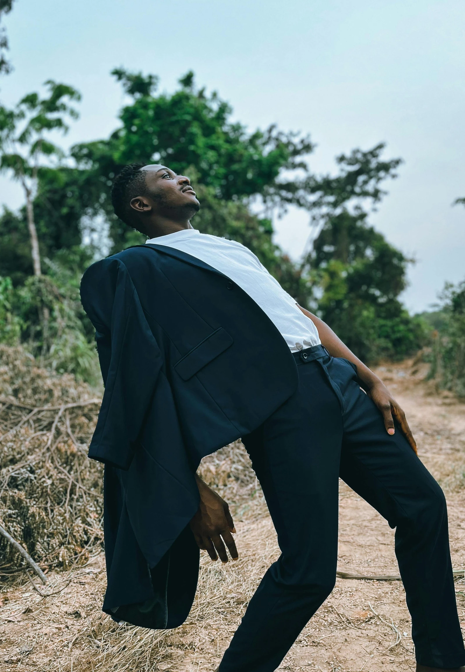 a man in suit and tie standing on dirt road next to a field