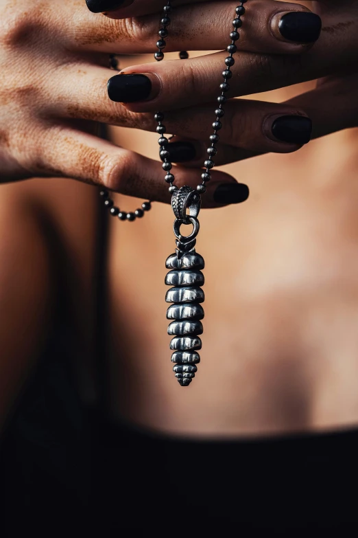 a woman with black nails is holding a silver pendant