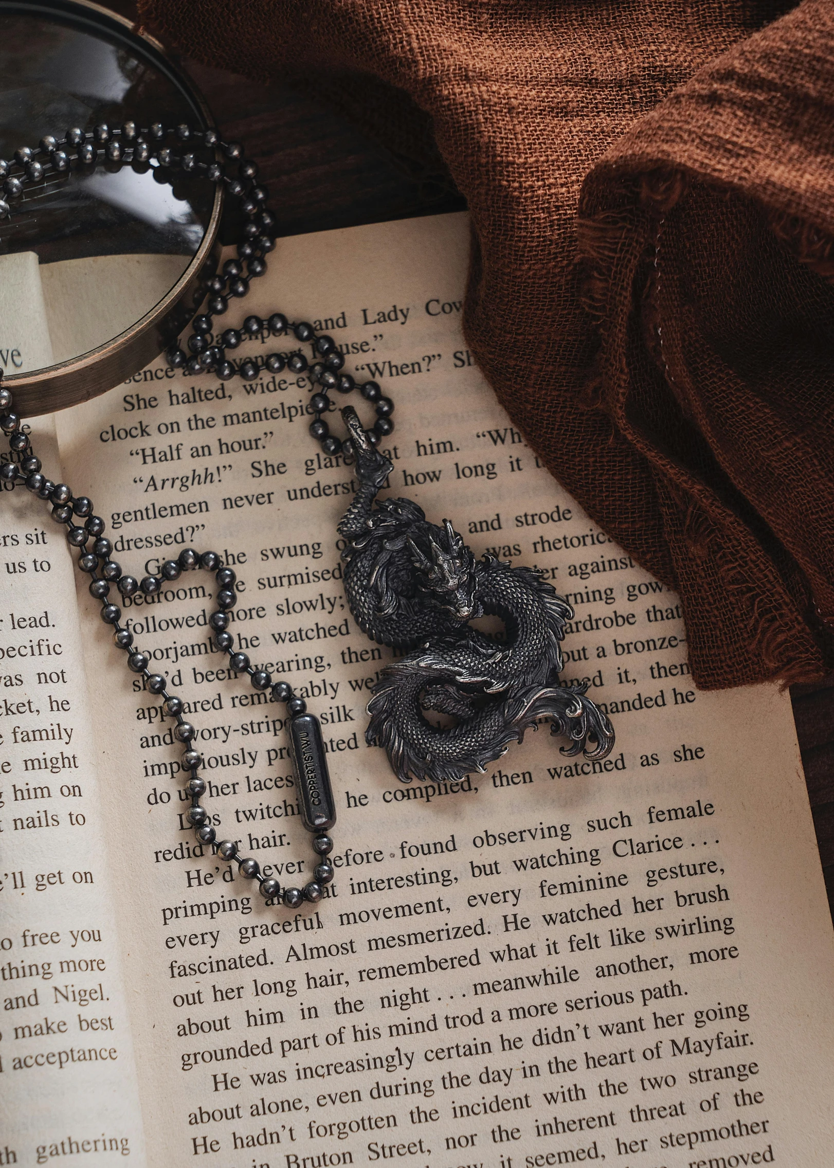 a black rosary with a glass of water, chain, and magnifying glass sitting on a book