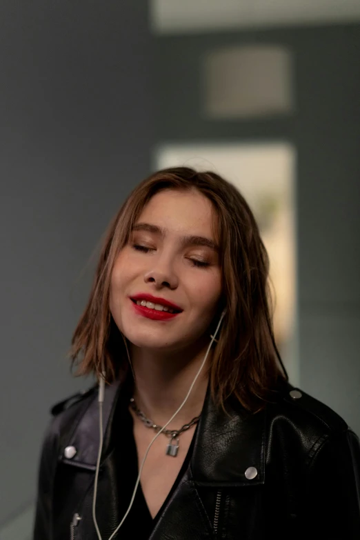 a woman wearing a leather jacket and earbuds looks away from the camera
