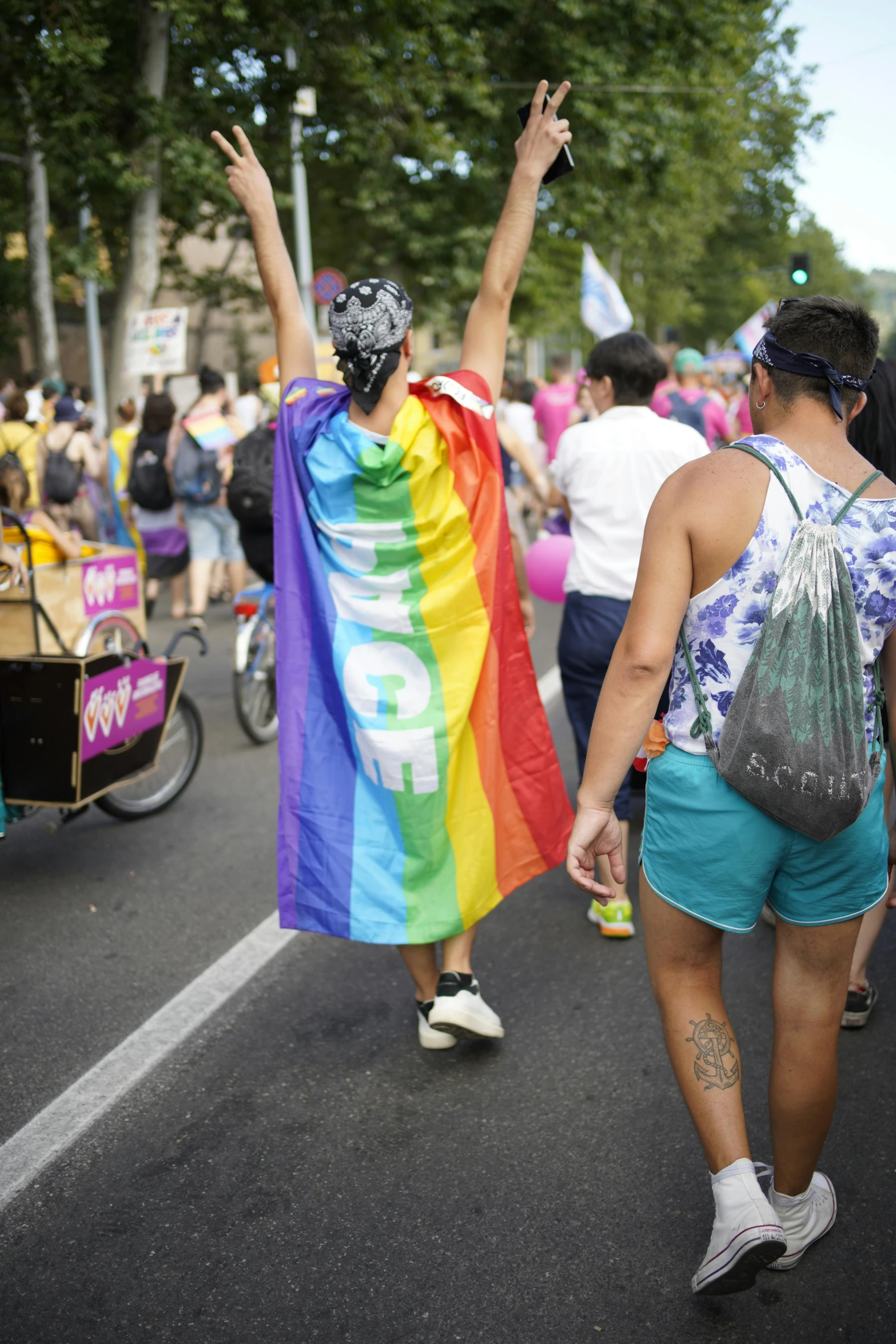 people walk in a parade with signs and a rainbow flag