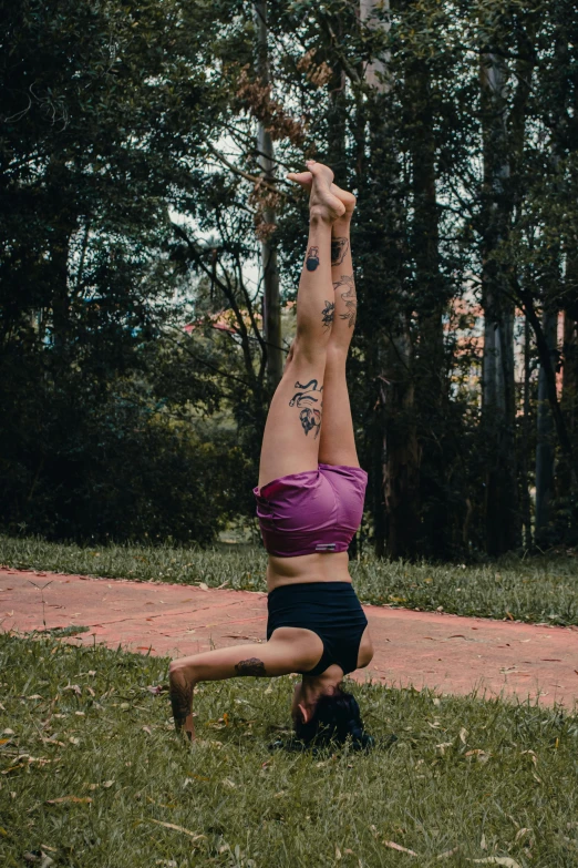 a woman in purple shirt doing yoga on grassy field