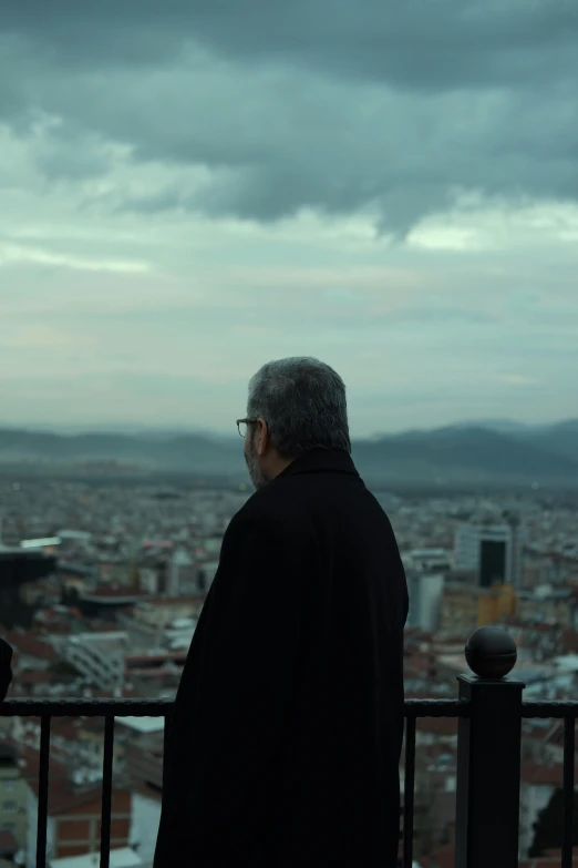 man overlooking large city under cloudy sky on balcony