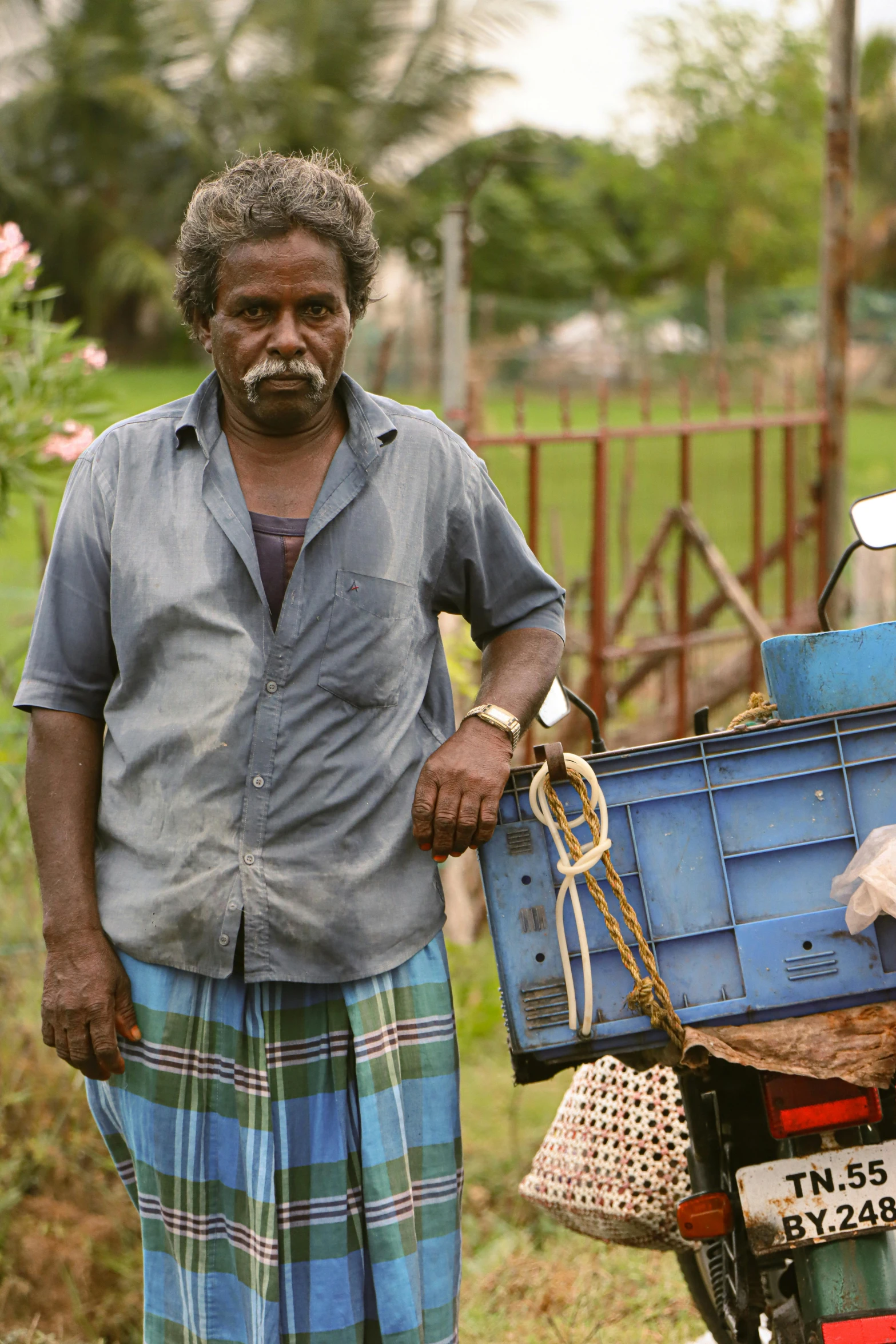 a man standing next to his parked motorcycle holding a blue crate