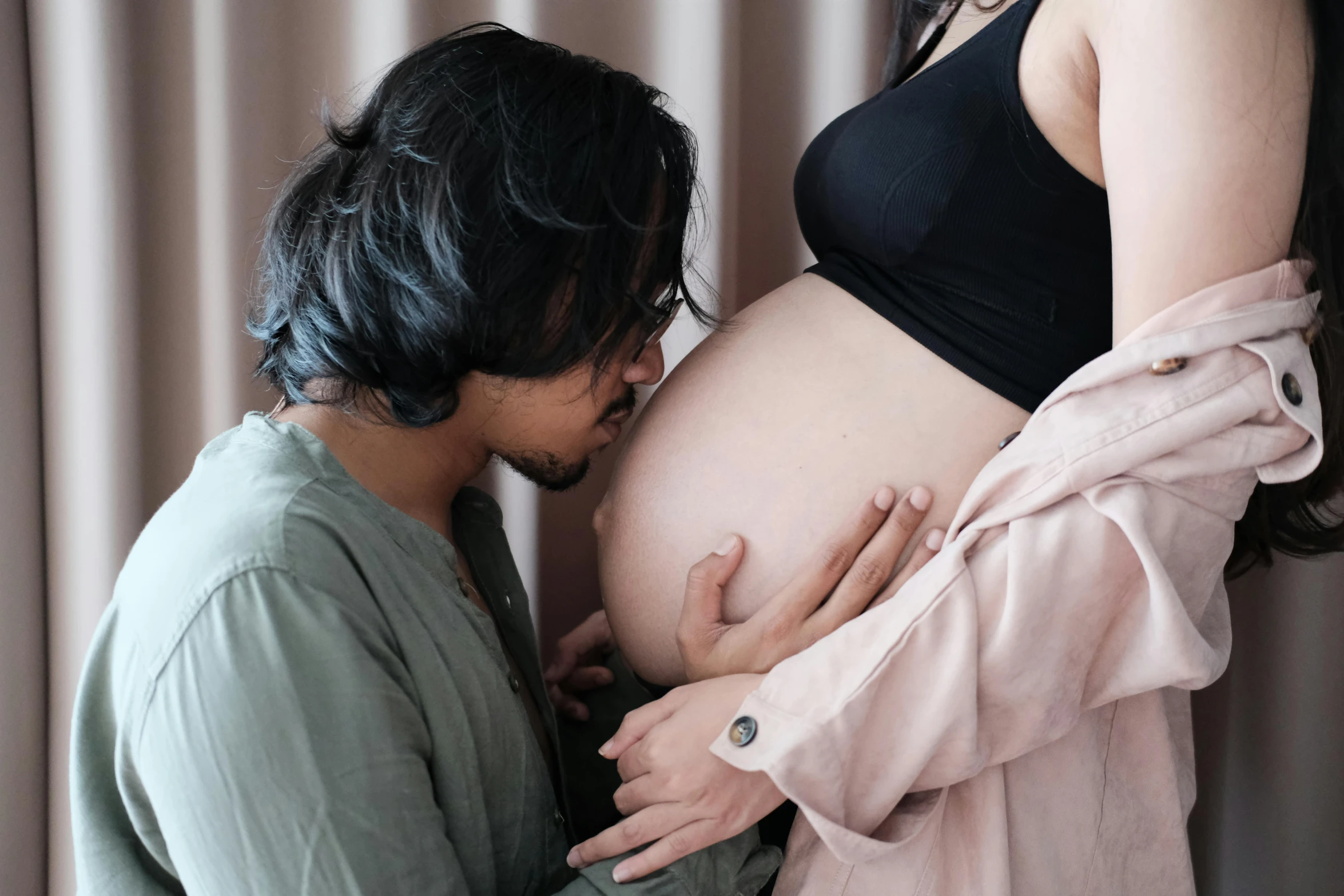 a pregnant woman wearing black clothes is holding her stomach while man wearing glasses is wearing black clothing