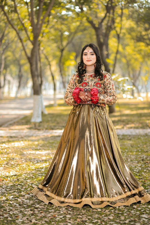 a woman wearing a gold dress and holding roses stands in the grass