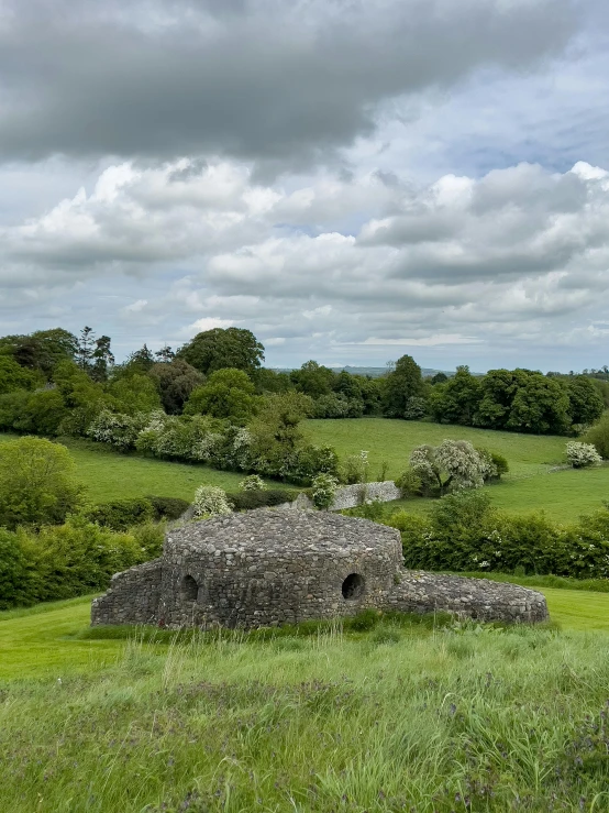 there is an old stone structure in the middle of the grassy field