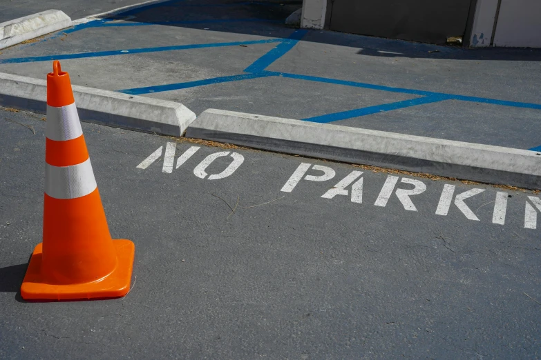 a cone that says no parking on a paved area with blue lines and buildings in the background