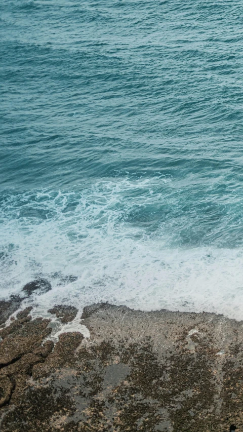 a man walking down a beach carrying a surfboard