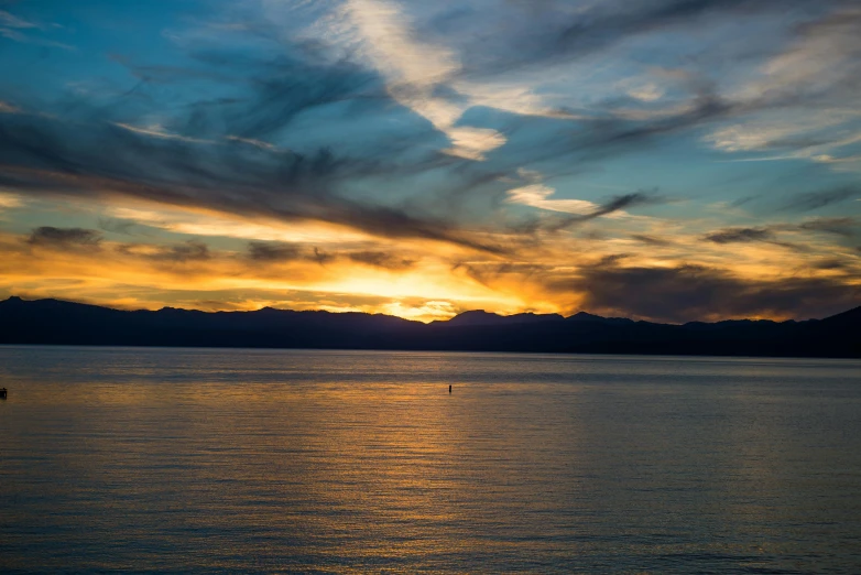 a cloudy sunset reflects in the water near mountains