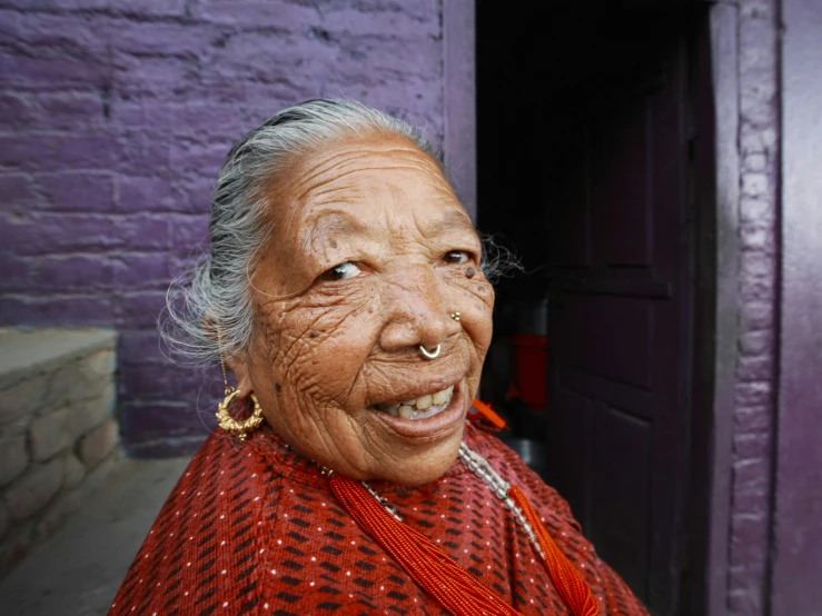 an old woman in red dress with nose rings looking off to the side