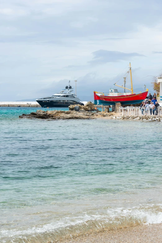 two boats are docked next to the shore as people walk on the sand