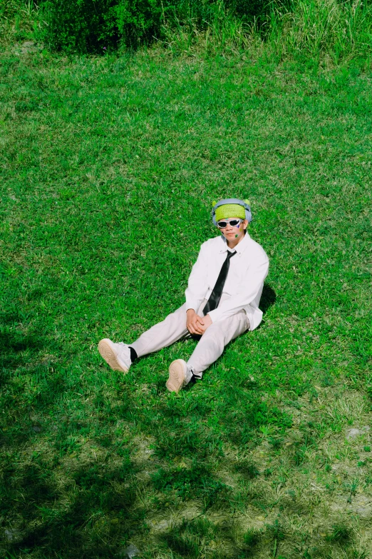 a man sits on a green field wearing a suit and tie