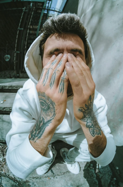 the man with tattoos covers his face and covers his hands with his hands