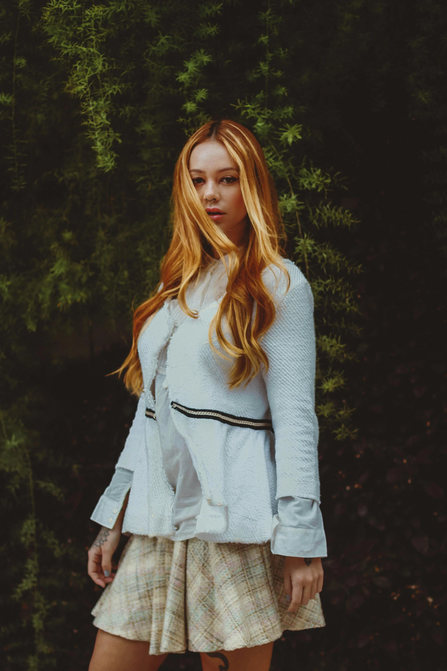 a young woman standing in front of a forest with her hands in her pockets