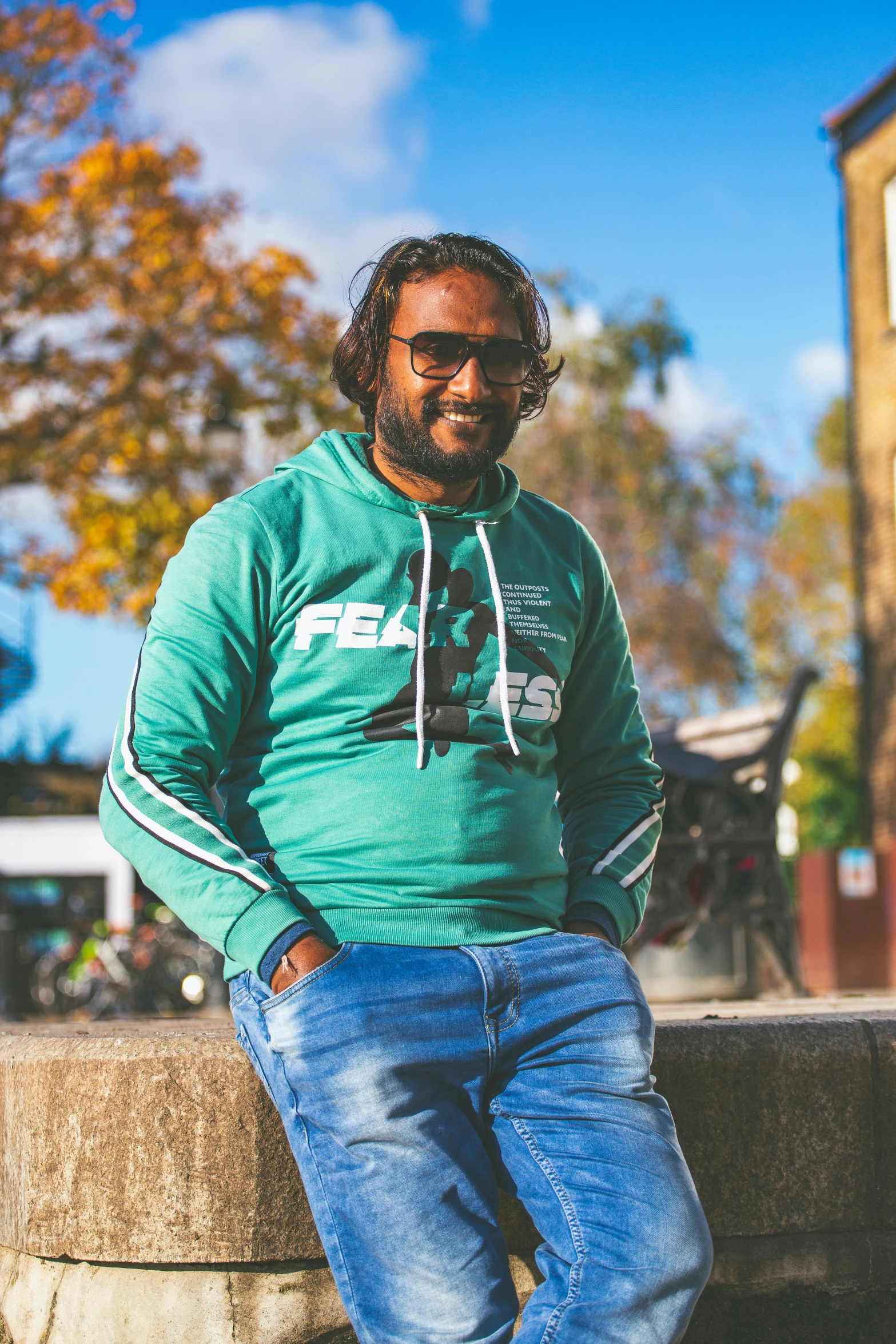 a man sitting on a ledge wearing jeans and sweatshirt