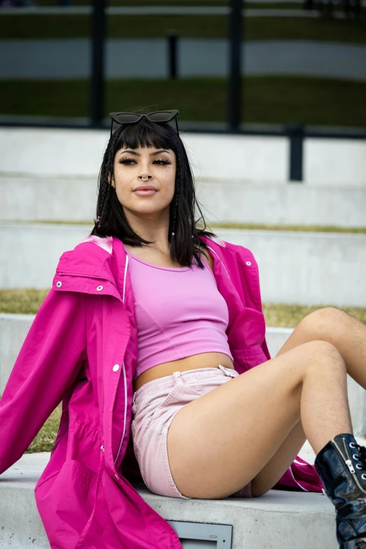 a girl wearing a pink top and short skirt is sitting on the concrete