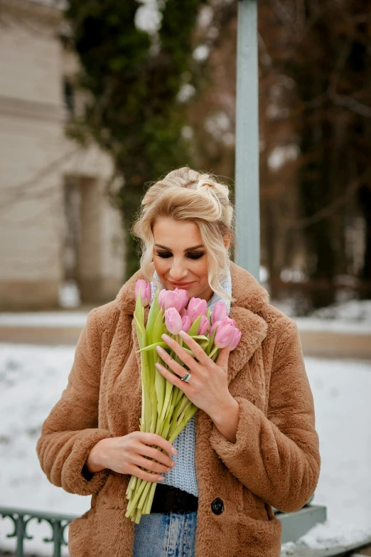 a woman in brown holding pink flowers and a coat