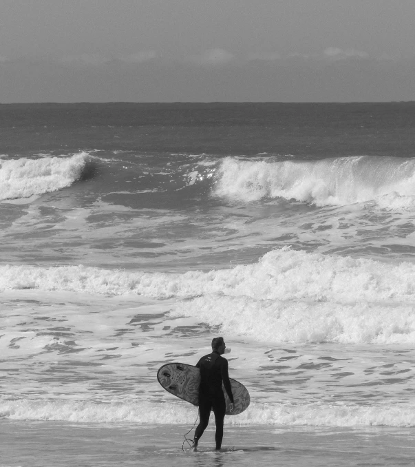 the man in the wet suit stands on the beach holding a surf board