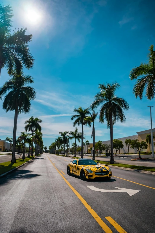 a yellow sports car drives down the street in the sun