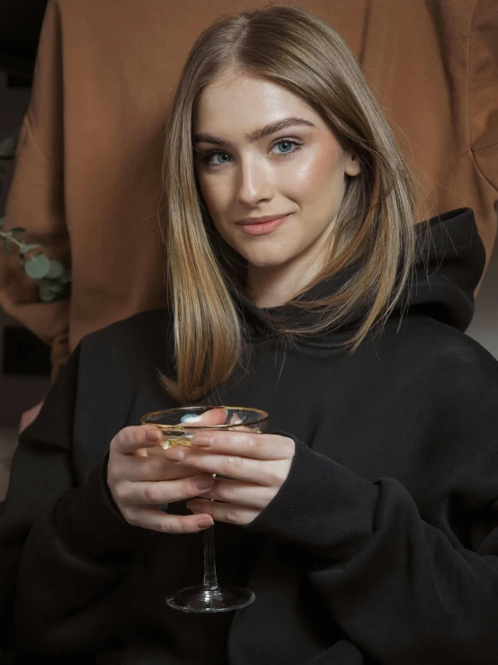 a girl in a black sweatshirt holds up a drink