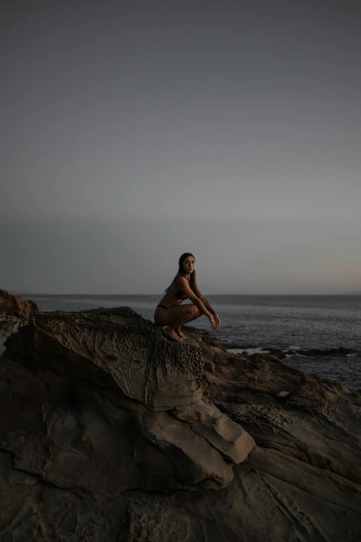 a woman poses on a rock in a wetsuit