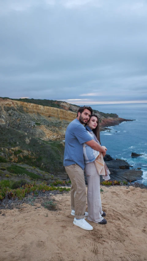 a man and a woman pose on the beach while holding each other