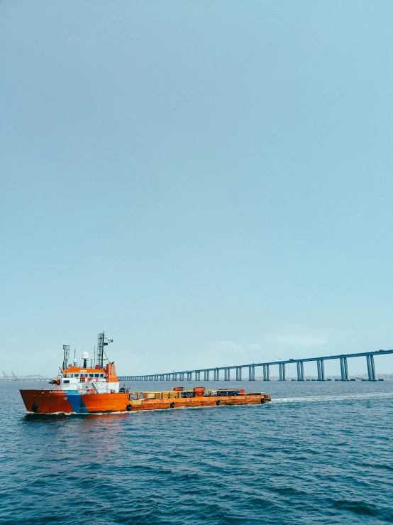 an orange tugboat traveling towards a large bridge