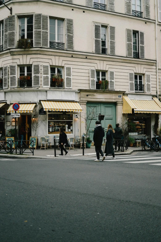 a city street has two people crossing a street in front of a store front