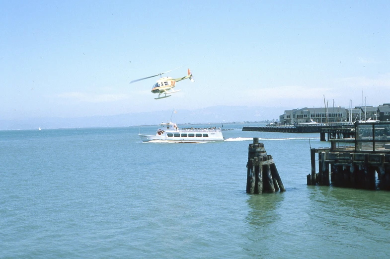 a boat floating by a pier with a helicopter flying above