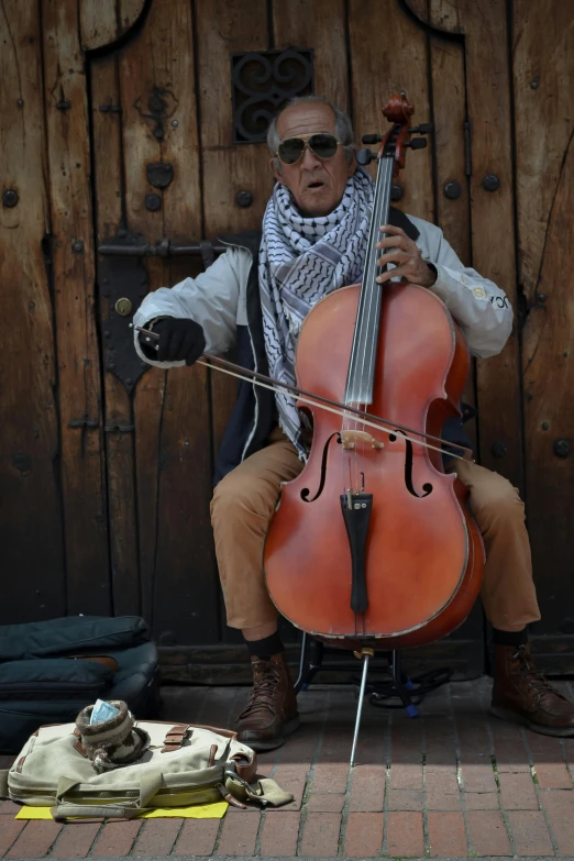 a man in black pants and sunglasses plays a cello