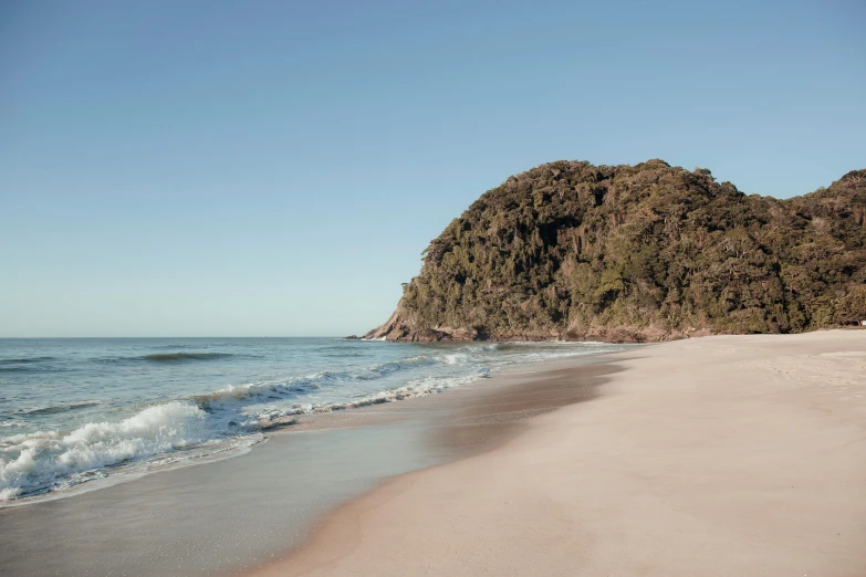 the sandy beach is next to a grassy hill