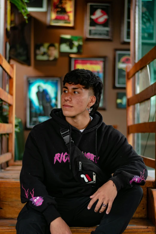 a male in a black hoodie sitting down and posing for the camera